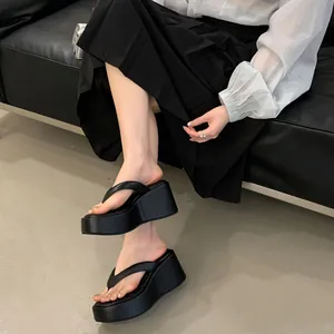 Detail of stylish black platform wedge thong sandals worn with a long pleated skirt