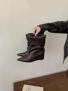 Detailed macro view of stylish brown pointed-toe slouchy wedge boots held by hand