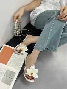 Detail of white square toe sandals with large orchid flower decoration and thin heels.