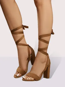 Primer plano de sandalias de ante marrón con tacón grueso y tiras cruzadas elegantes