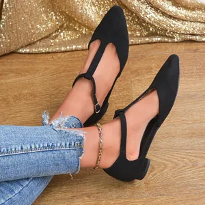 Elegant women's black suede T-strap flat shoes with pointed toe on wooden floor.