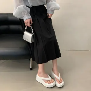 Model wearing stylish white platform thong sandals paired with a black pleated skirt for summer.