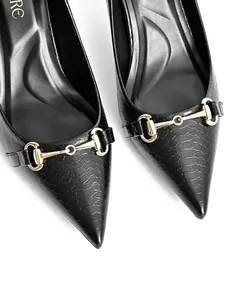 Macro view of black crocodile pattern pointed-toe shoes with an elegant gold metal buckle