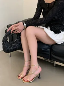 Close-up of elegant gold strappy high-heel sandals with square toe on model's feet.