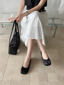 Detailed shot of black Tabi split-toe flats with bow on model in a modern interior.
