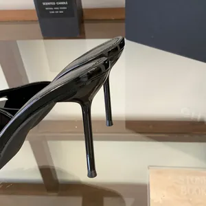 Detailed view of the sleek black patent leather stiletto heel on elegant women's high-heel mules