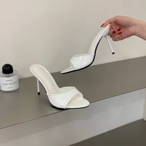 Close-up of elegant white patent leather stiletto high heel sandals with open toe.