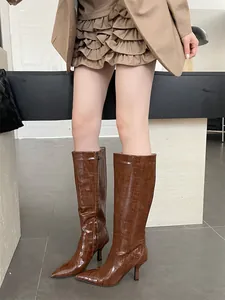 Elegant detail view of brown crocodile embossed knee-high boots featuring stiletto heels