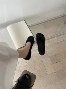 Close-up detail view of black split-toe ballet flats with bow decoration on a glass table