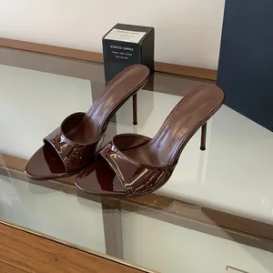 Detailed view of glossy chocolate brown stiletto mules on a reflective glass surface