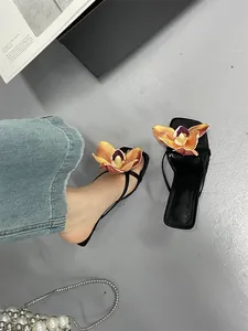 Detailed view of black thong sandals with large orange flower embellishment and straps