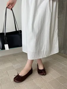 Close-up of elegant brown split-toe Tabi ballet flats with bow detail on a white tiled floor.