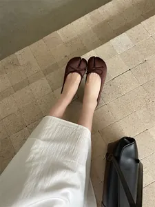 Detailed view of brown split-toe tabi flats with bow decoration on stone tiles.