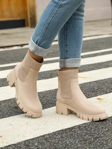 Stylish close-up of beige knit Chelsea boots with chunky heels on a street crossing.