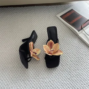 Elegant black thong sandals with large peach orchid flower detail on white textured rug