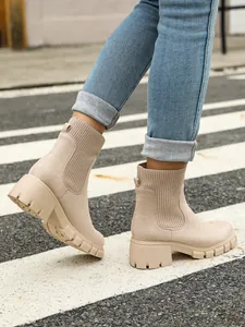 Close-up detail of beige chunky knit Chelsea boots worn with blue jeans on city street.