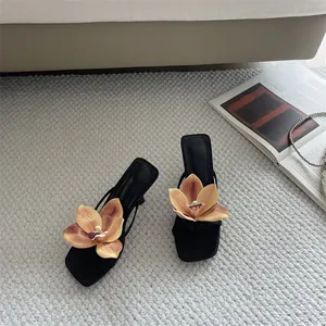 Detailed high-angle view of black orchid flower sandals on a textured gray carpet