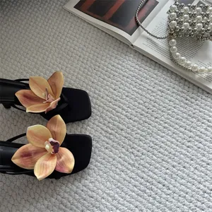 Detailed view of elegant orchid flower design on French style black thong sandals