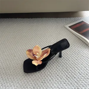 Detail view of black square-toe heeled sandal with oversized peach flower decoration