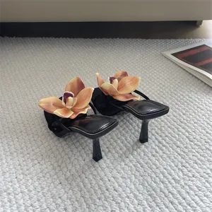 Detailed view of black square-toe thong sandals featuring large orchid floral decoration