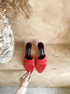 Dettaglio ravvicinato di sabot in camoscio rosso con borchie argentate eleganti