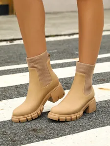 Detail view of beige knitted Chelsea boots with chunky heels on a zebra crossing.