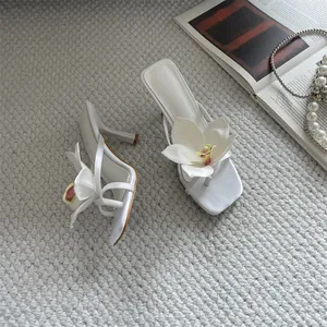 Elegant white thong sandals featuring oversized flower detail and slim high heels.