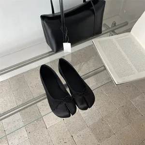 Elegant black split-toe ballet flats with bow detail on a glass table