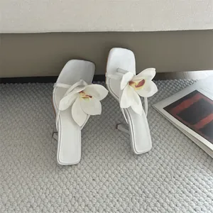 Detail of white square toe sandals with large 3D flower and slim high heel.
