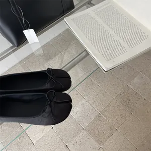 Detailed view of black split-toe tabi flats featuring a delicate bow and matte finish