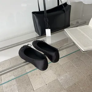 Detailed view of black split-toe Tabi ballet flats with bow accent on glass shelf