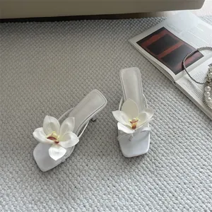 Detailed view of elegant white high-heel thong sandals featuring 3D orchid flower decor.