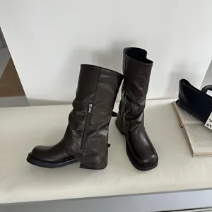 Nahaufnahme brauner mittelhoher Hosenstiefel mit Reißverschluss auf einer weißen Bank.