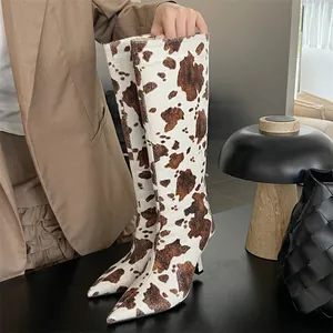 Chic brown and white cow print knee-high boots with a pointed toe and thin stiletto heels.