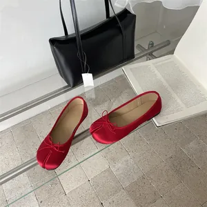 Macro detail view of elegant red satin Tabi ballet flats with bow on a glass surface.
