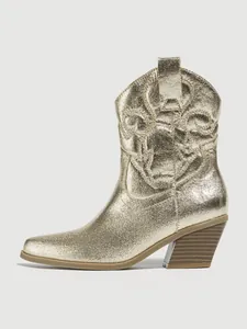 Detailed macro view of metallic gold western boot with embroidered patterns and block heel.
