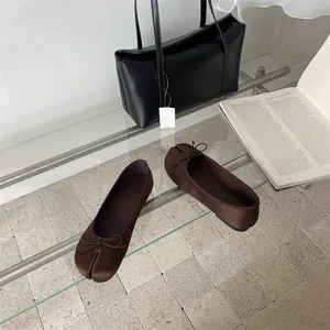 Detail view of stylish brown tabi split-toe flat shoes with a bow detail on glass table