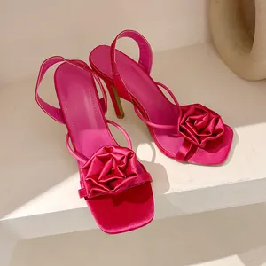Close-up of hot pink satin sandals featuring a delicate fabric rose on the toe strap.