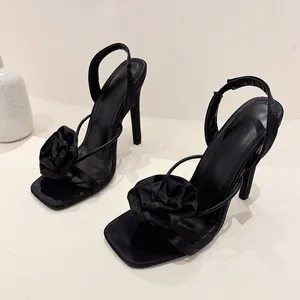 Detail view of black silk sandals with delicate flower embellishment and square toe.