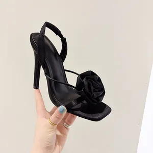 Detailed view of elegant black satin high heel sandals featuring a large 3D flower decoration.
