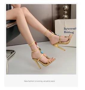Nahaufnahme goldener High-Heel-Sandalen mit bunten Steinen am T-Riemen-Design