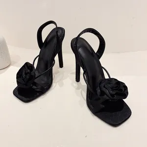 Macro view of black satin high-heeled sandals with elegant rose flower detail.