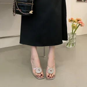 Close-up of transparent PVC sandals with sparkling rhinestone buckle on a model.