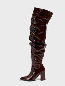 Close-up of glossy burgundy patent leather over-the-knee boots with wrinkled texture
