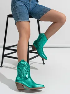 Detail of metallic green western boots with embroidery and chunky heel on a model