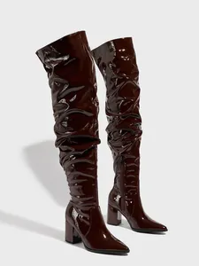 Close-up of dark brown patent leather slouchy thigh-high boots with chunky heels.