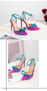 Close-up view of magenta satin high heels with emerald green bow and ankle strap