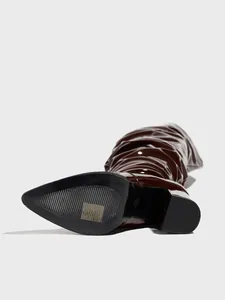 Detail view of the non-slip sole and block heel of a glossy brown patent leather boot