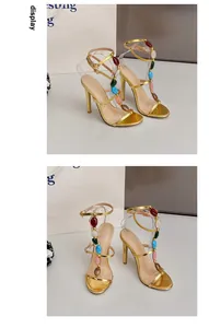 Nahaufnahme eleganter goldener High-Heel-Sandalen mit buntem Stein-T-Steg-Verzierungen