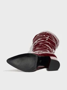 Detail view of burgundy shiny patent leather pleated boots with pointed toe and block heel